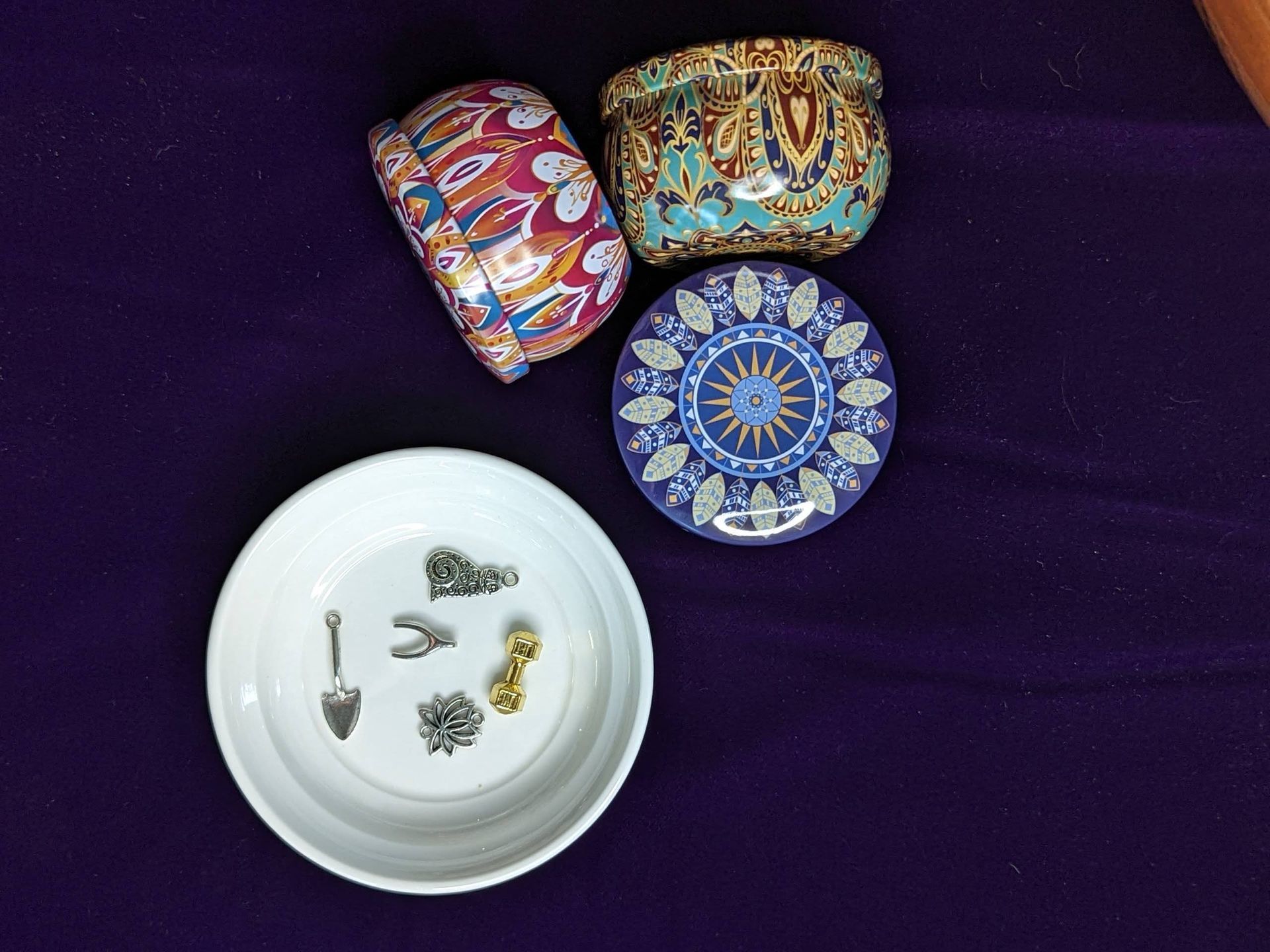 Decorative rings and earrings in a white dish beside colorful patterned boxes on a purple cloth
