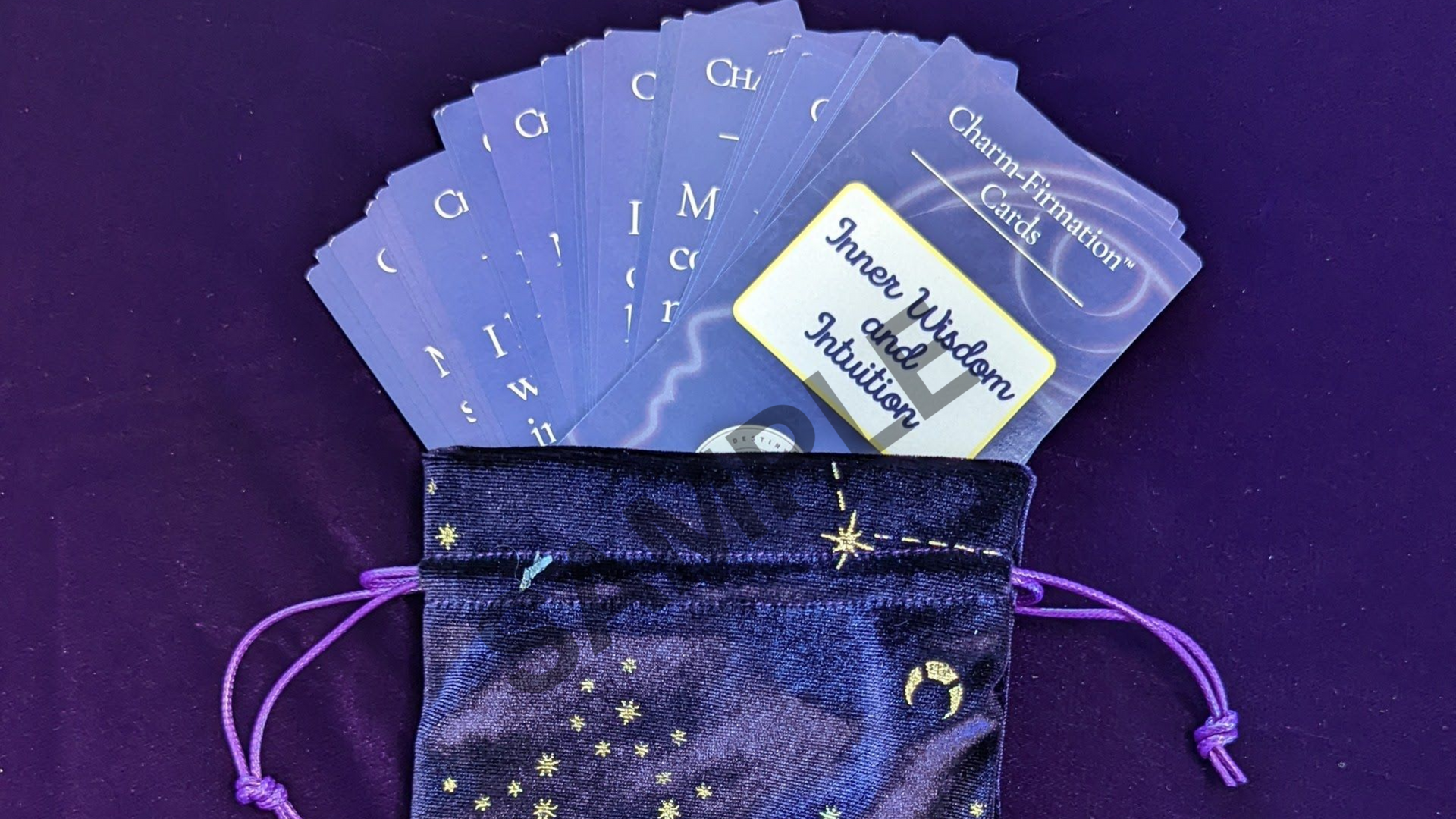 Purple drawstring pouch holding blue illustrated cards and a small box on a purple background