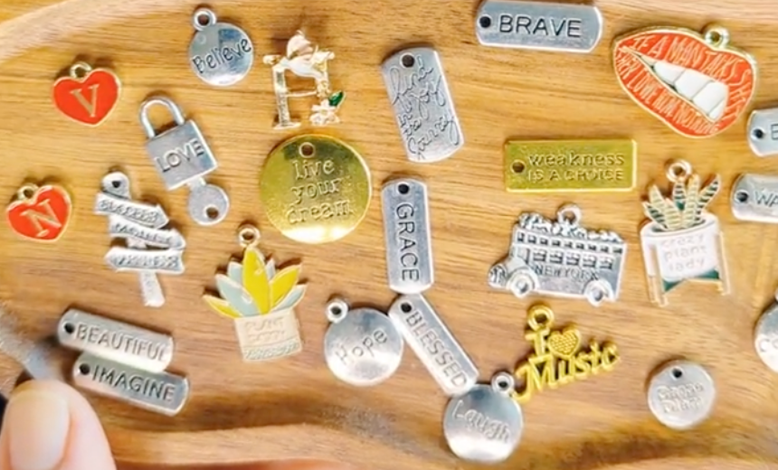 Collection of colorful charms on a wooden tray including words and letters like grace, blessed, brave, imagine, and more