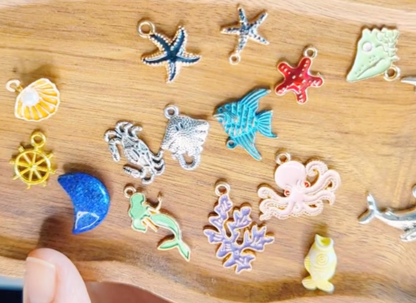Collection of colorful charms on a wooden tray including ocean creatures and symbols like star fish, stingray, crab, and more