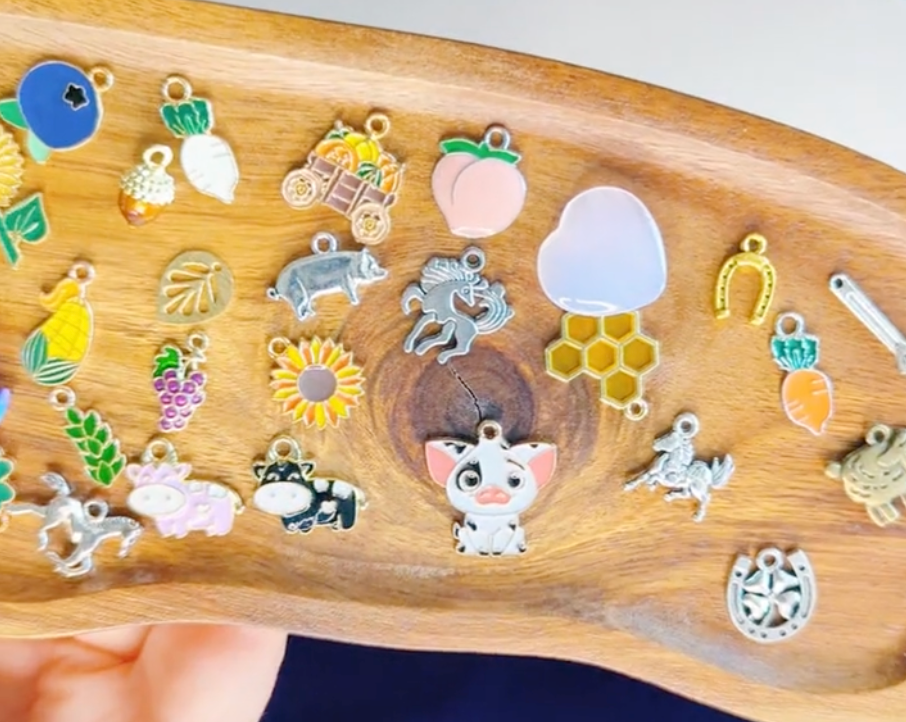 Collection of colorful charms on a wooden tray including farm charms like cow, pig, sunflower, bees, corn, and more