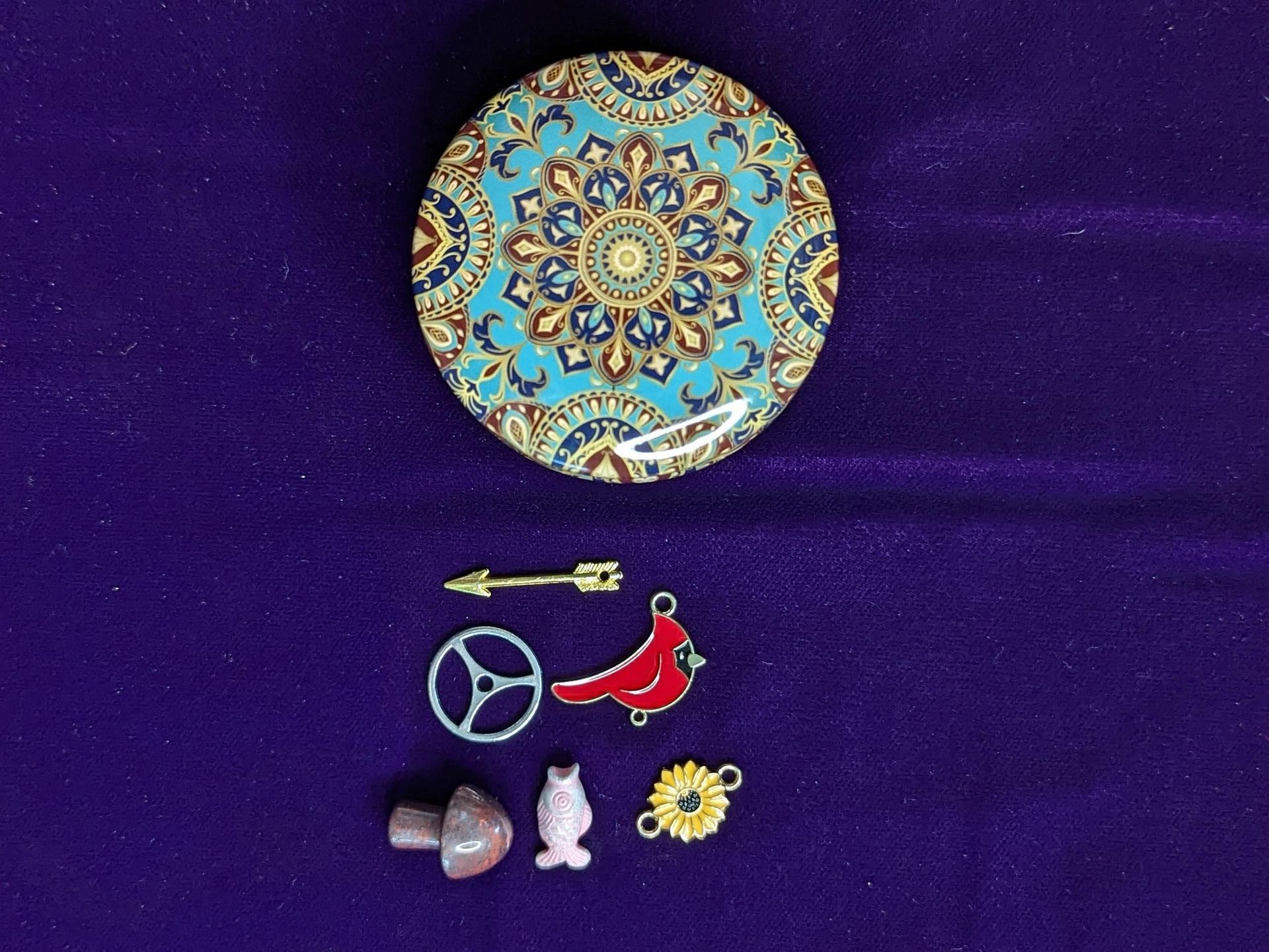 Keepsake tin container with a sample of charms including arrow, red cardinal, and other charms

