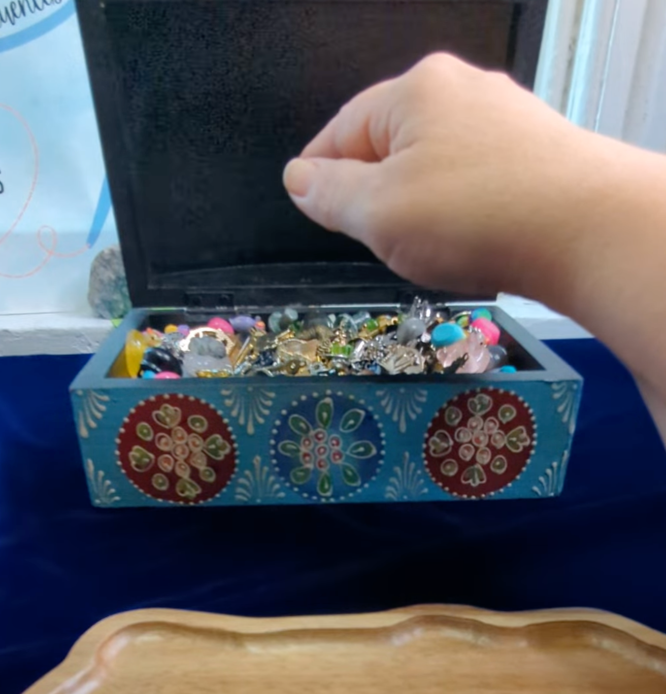 Hand reaching into a turquoise charm box filled with charms