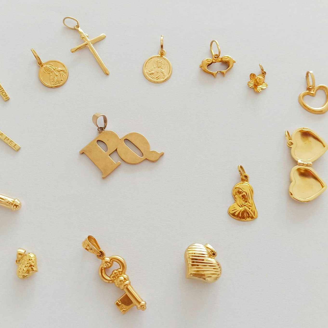 Gold jewelry charms and pendants arranged on a light background.