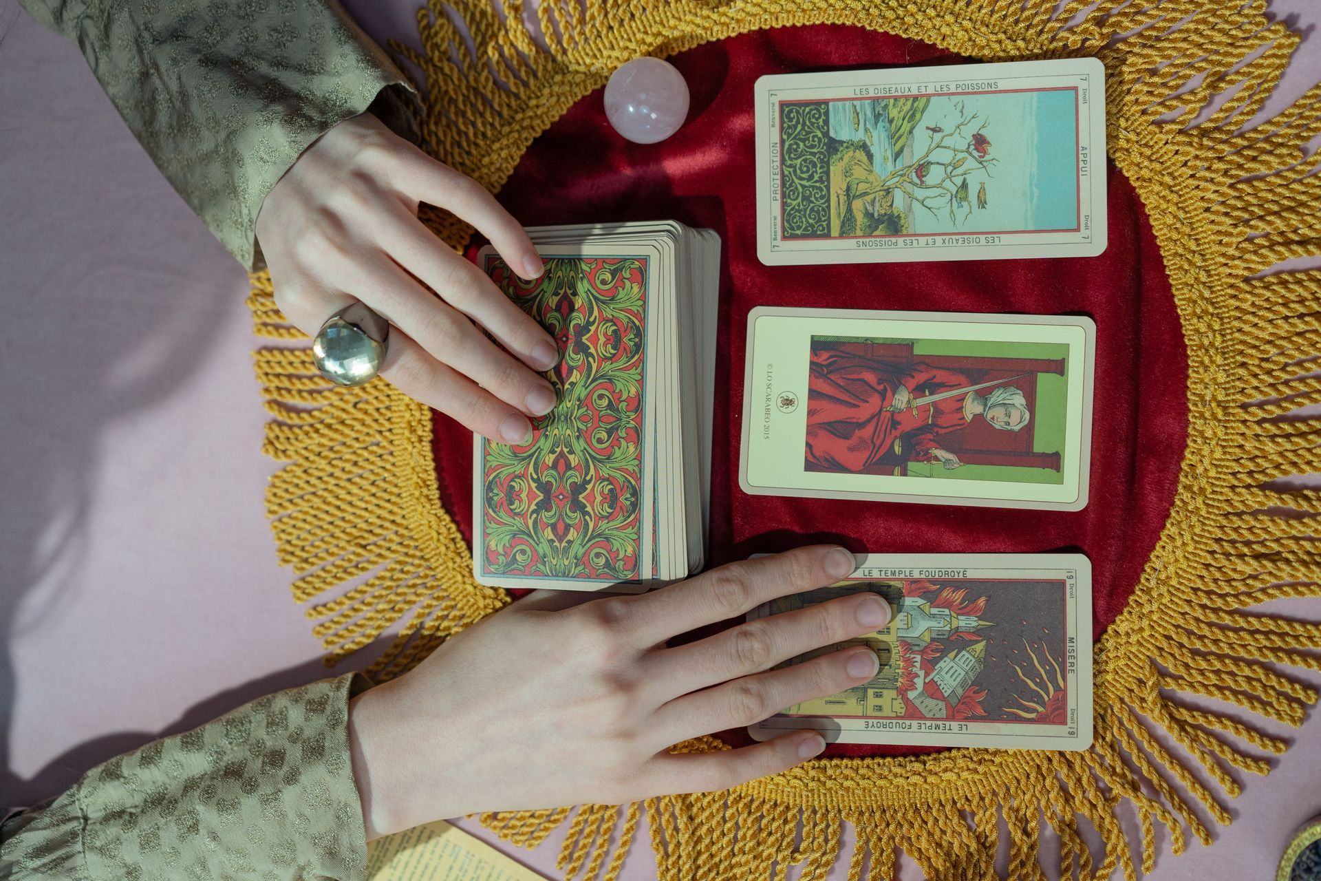 two hands with tarot cards showing on a red velvet cloth