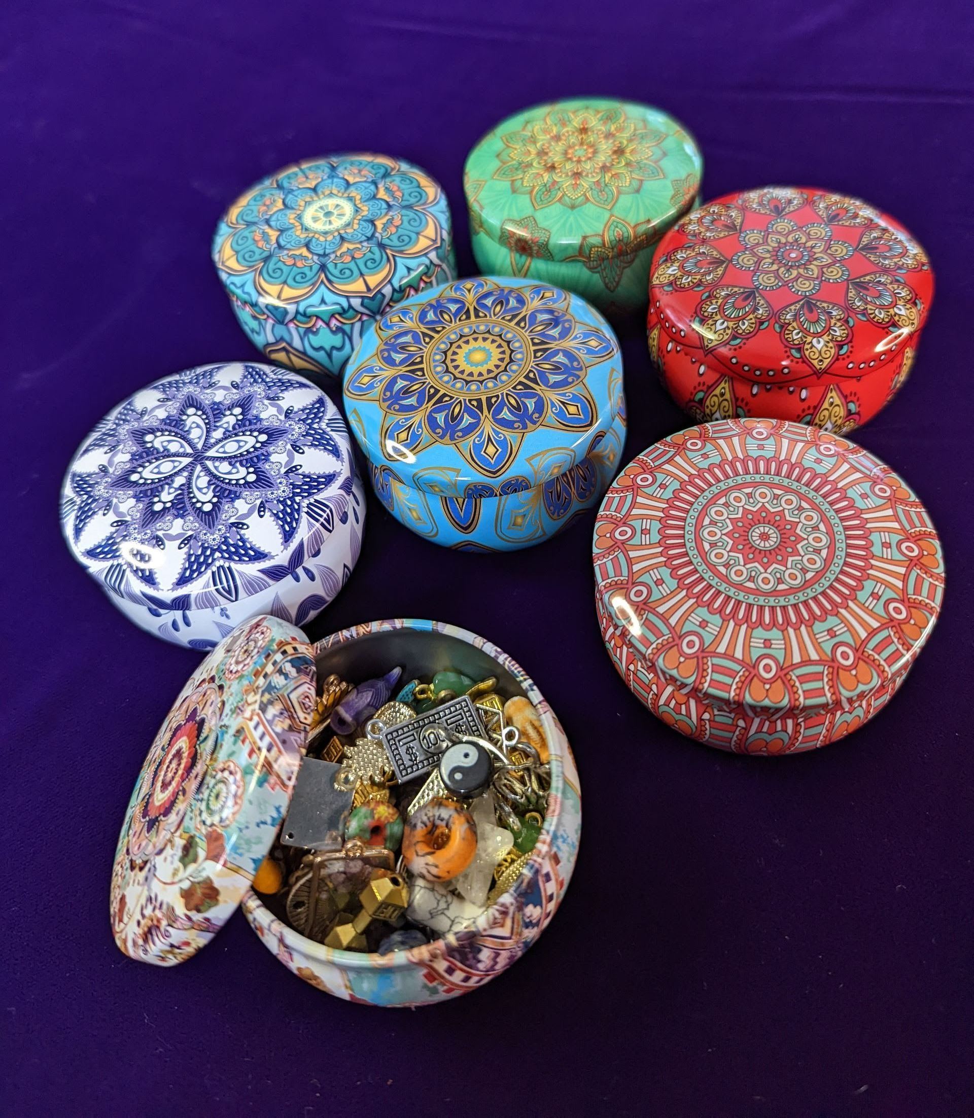 Colorful round decorative boxes with ornate patterns on a purple background, one open showing assorted trinkets