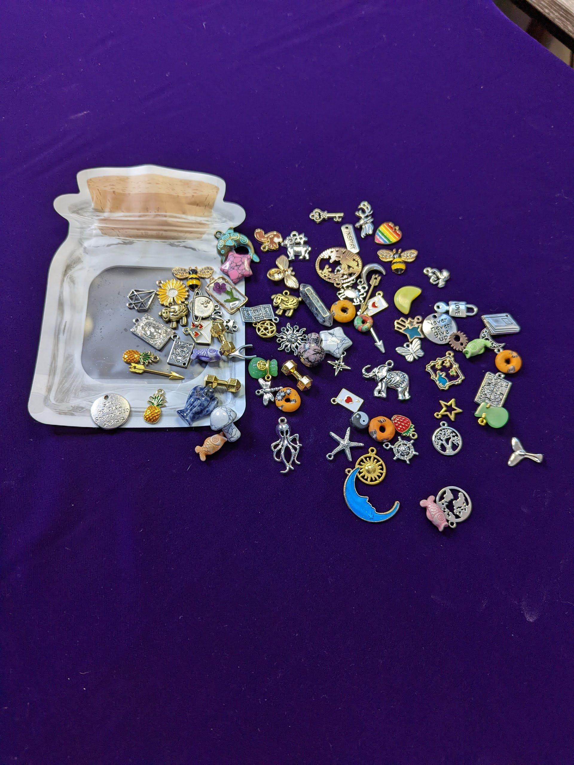 Small clear pouch spilling colorful enamel pins and charms onto a purple surface
