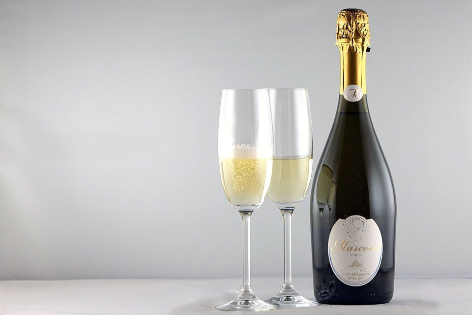 Bottiglia di champagne con due flûte piene su sfondo grigio chiaro