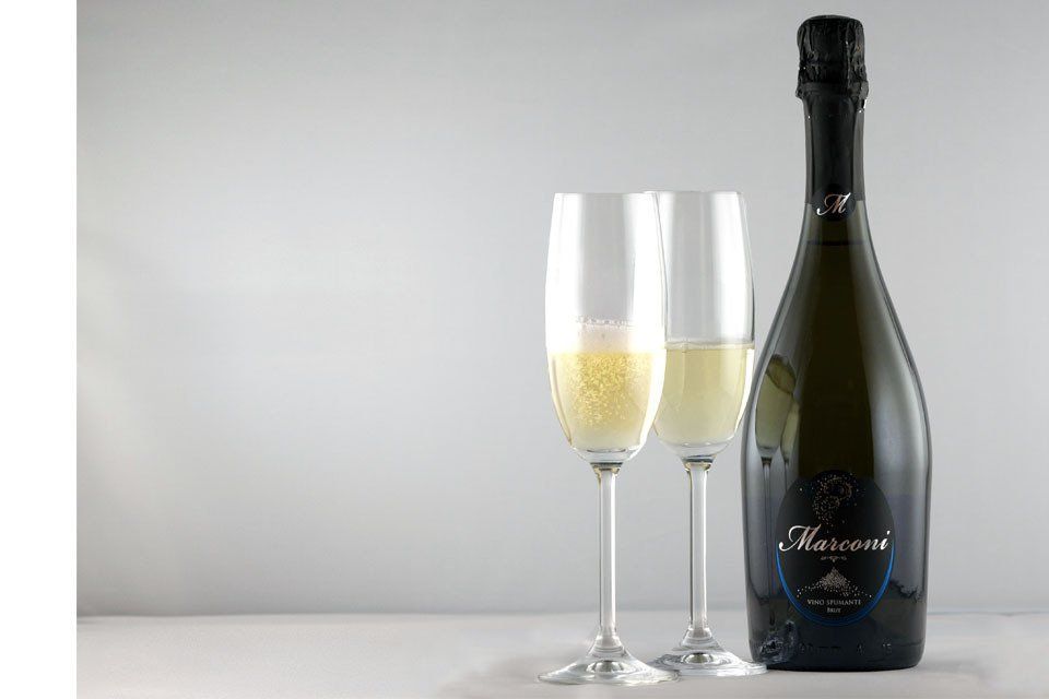 Bottiglia di champagne accanto a due flûte piene su uno sfondo grigio chiaro.