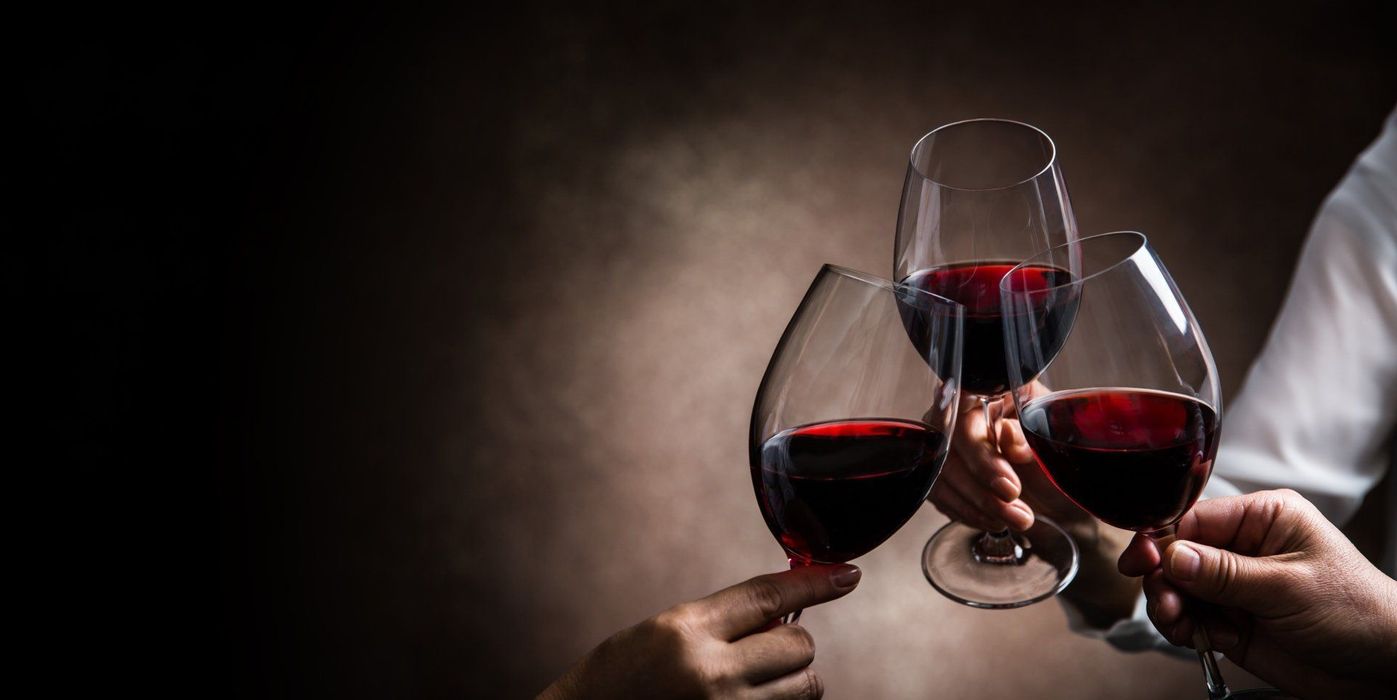 Tre mani fanno tintinnare calici di vino rosso su uno sfondo scuro