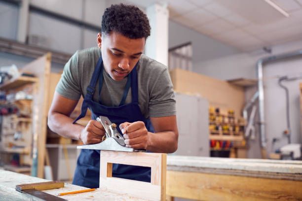 Young carpenter using hand plane on wood