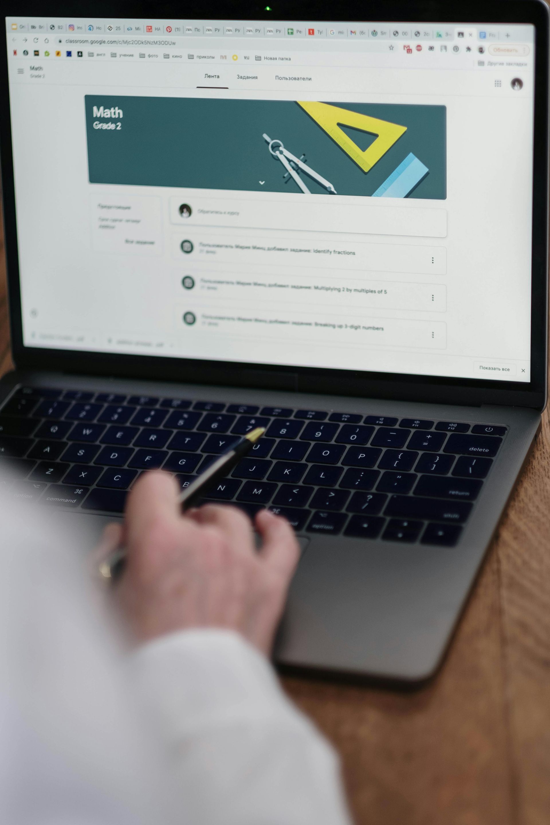 A person using a stylus on a laptop displaying a Math Google Classroom page with geometric icons in the banner.