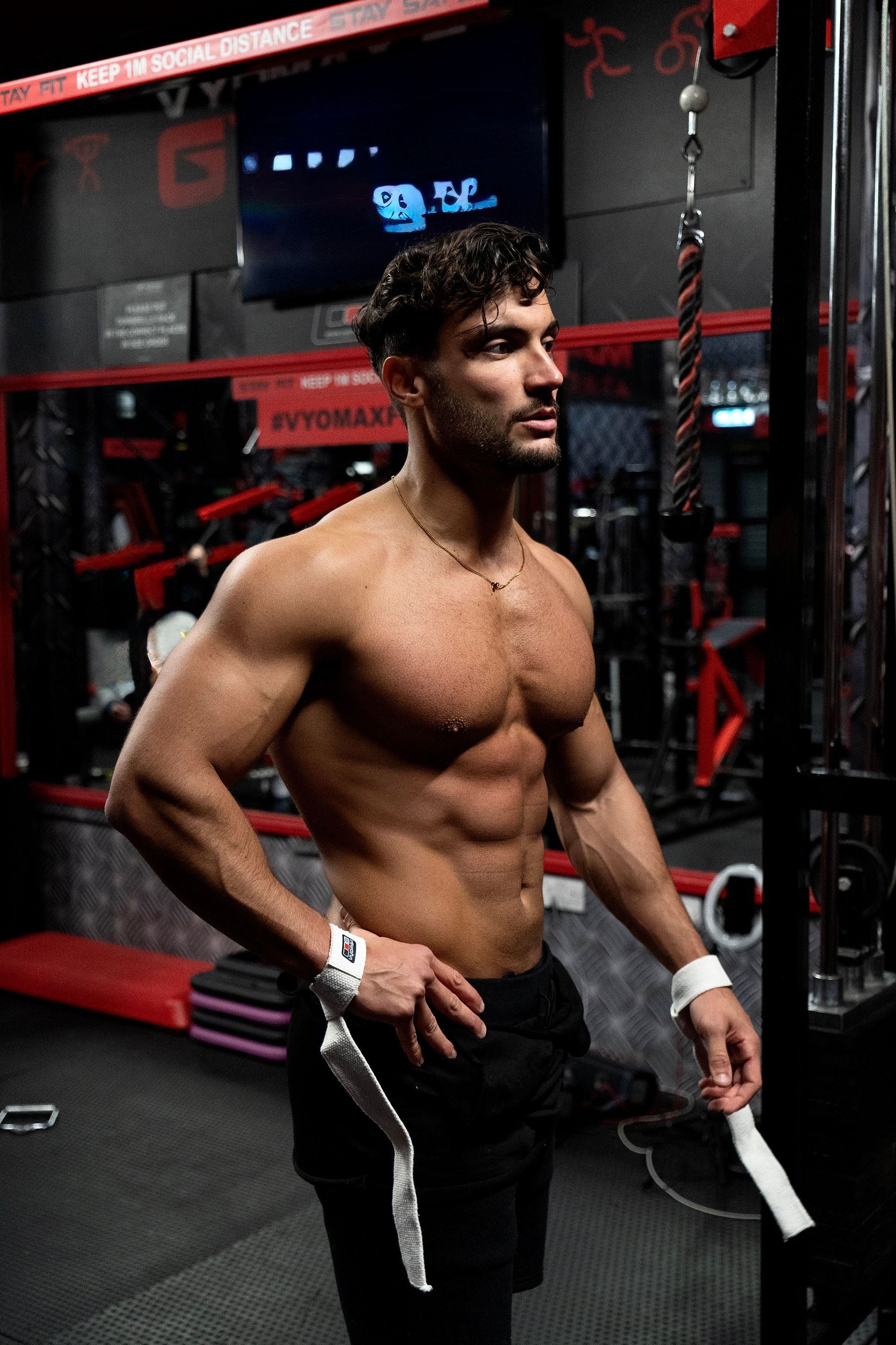 Davide in a gym, looking away. Wearing wrist wraps and black shorts.
