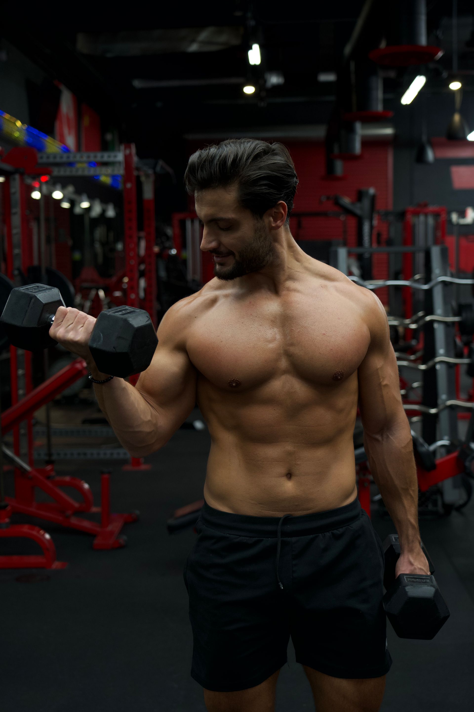 Davide with muscular physique doing bicep curls with dumbbells in a gym.