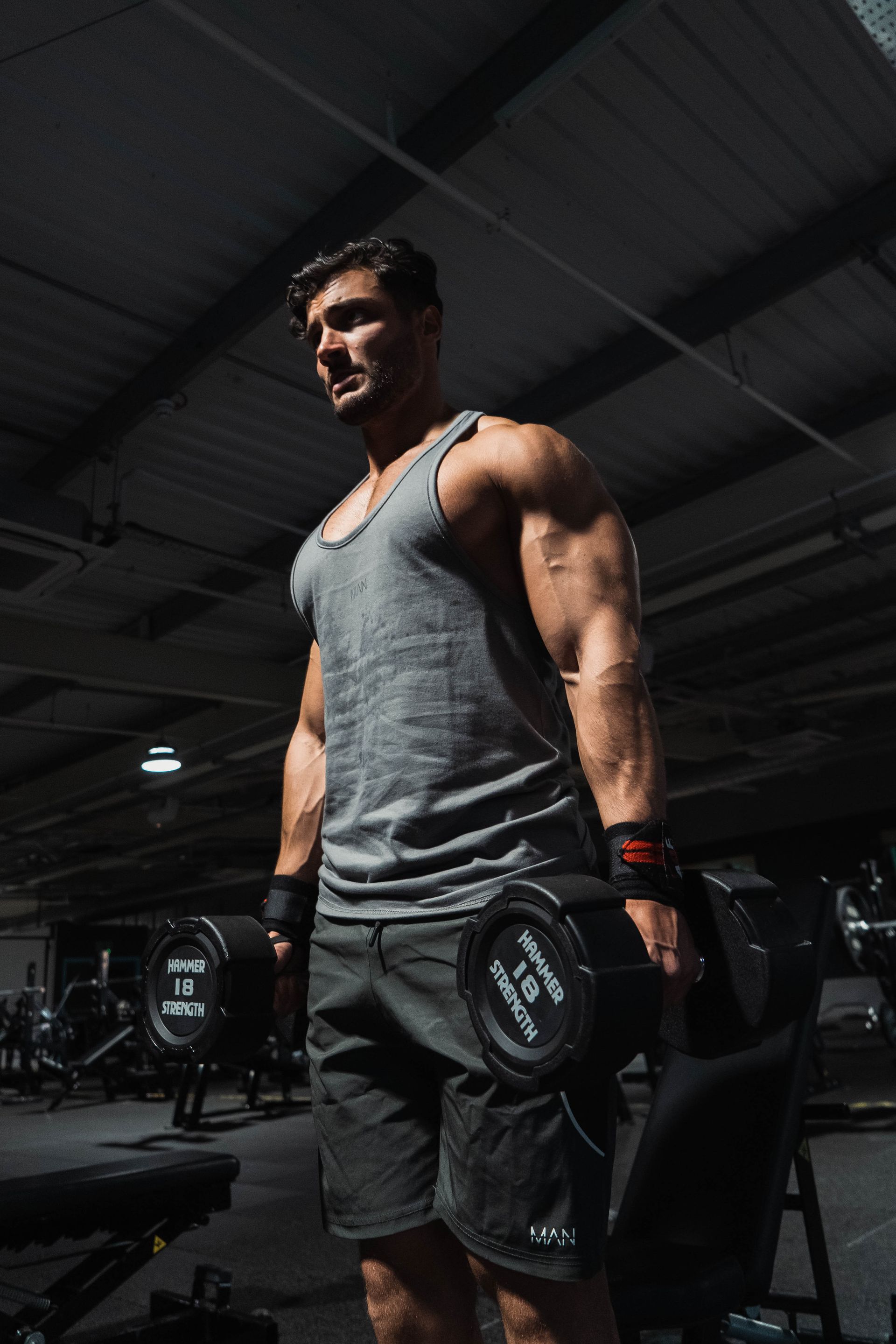 Davide in gym lifting dumbbell, dark setting.