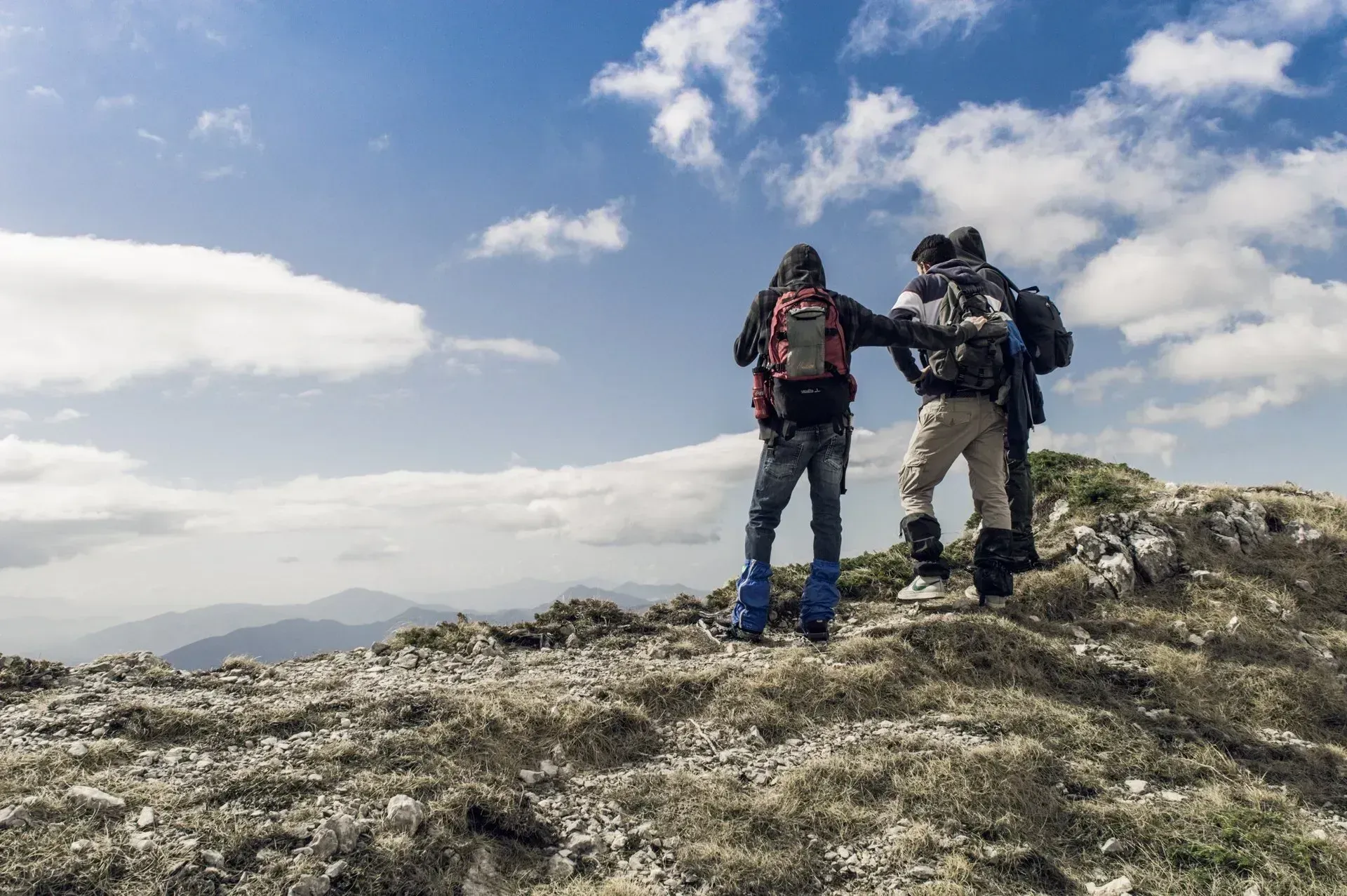 Hikers on a mountain peak looking out at a scenic view under a cloudy sky.