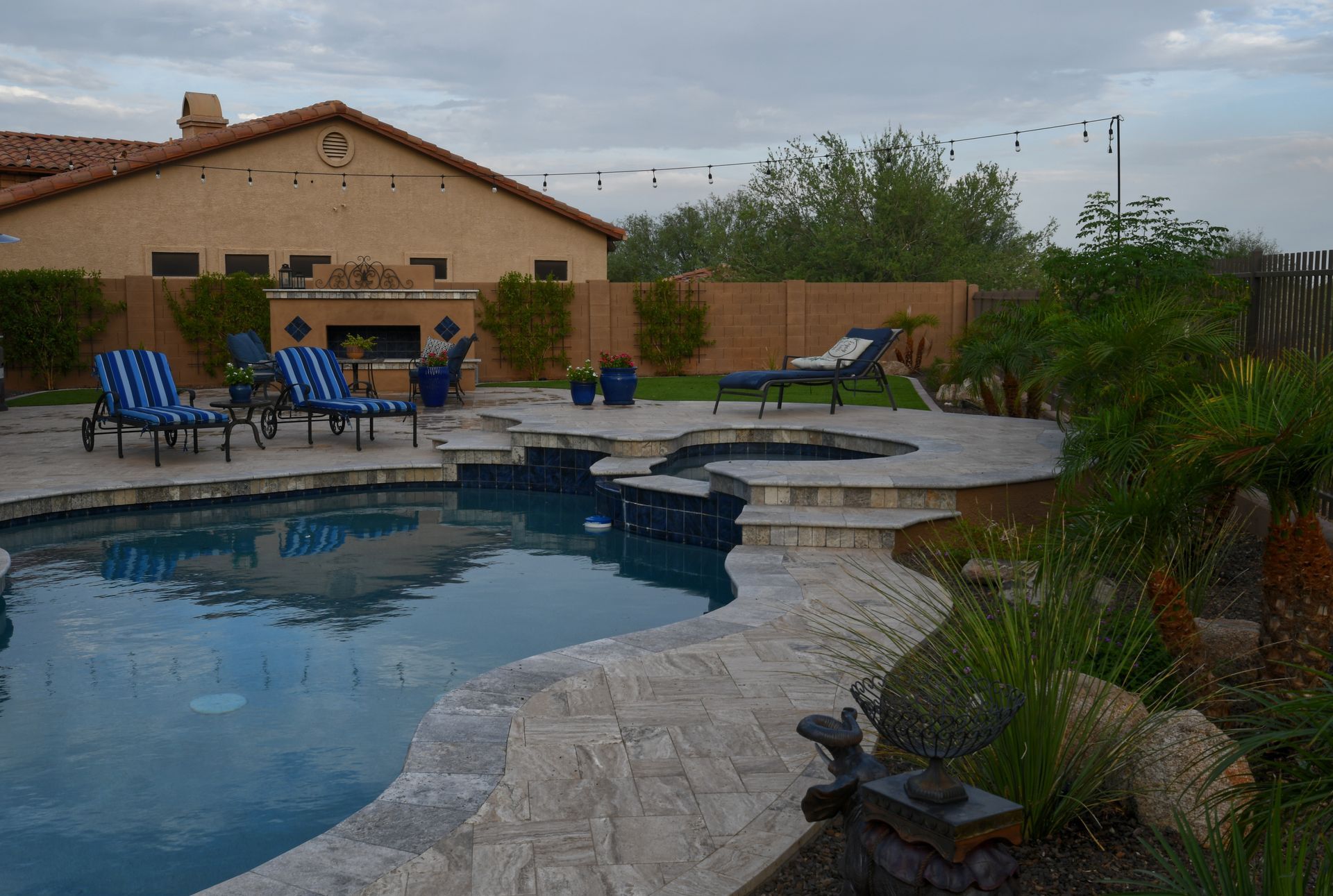 Backyard pool with a tiled spa, striped lounge chairs, and stone patio at dusk.