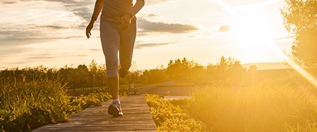 Person running on a wooden path with bright sunlight in the background.
