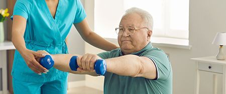 A healthcare worker helps an older adult exercise with dumbbells.