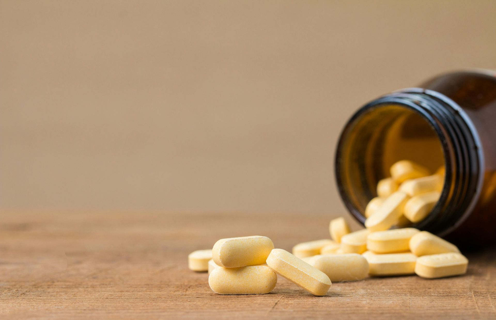 Yellow pills spilling from a brown bottle on a wooden surface.