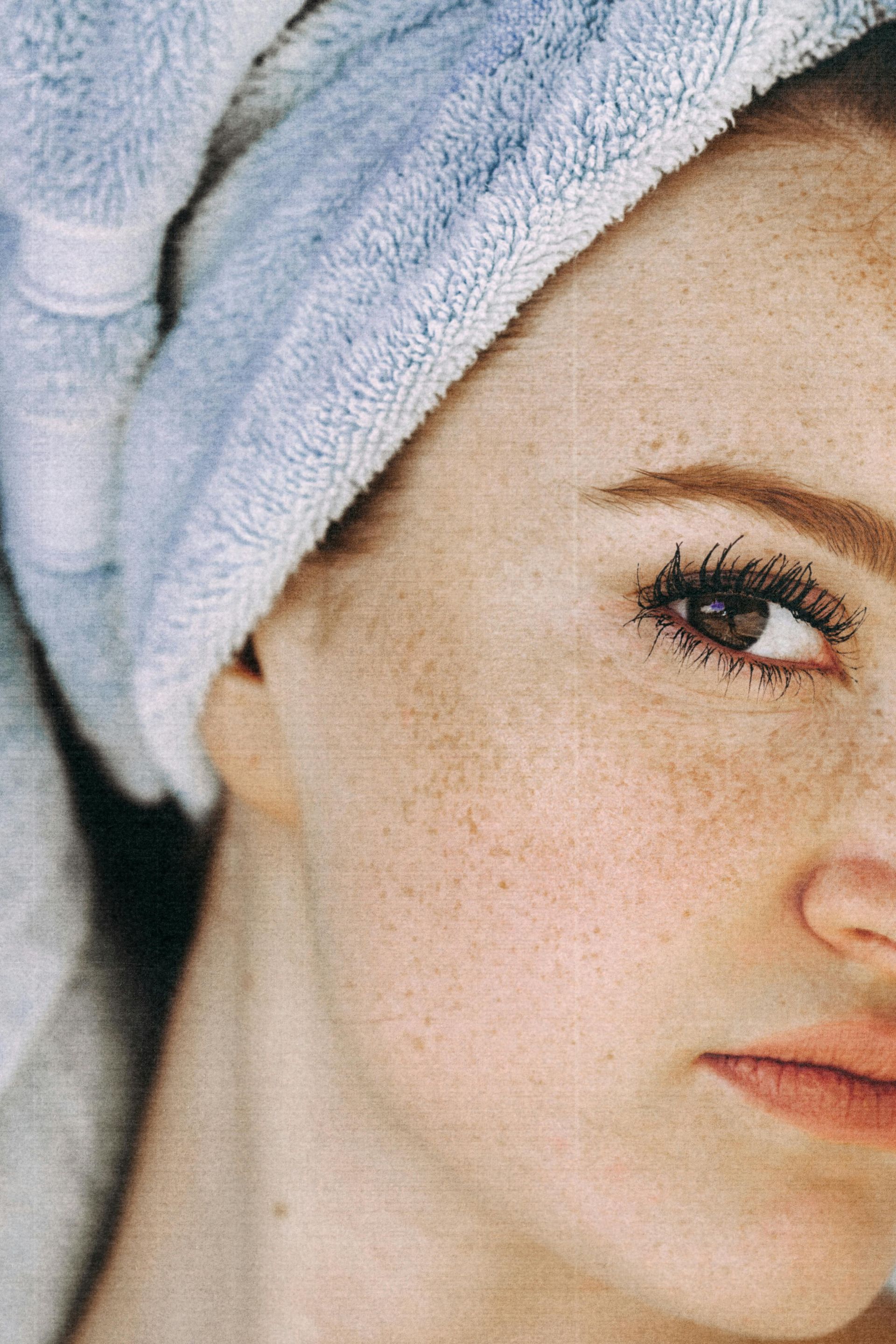 Woman with light skin, many freckles, wrapped in a blue towel. Looking at the camera.