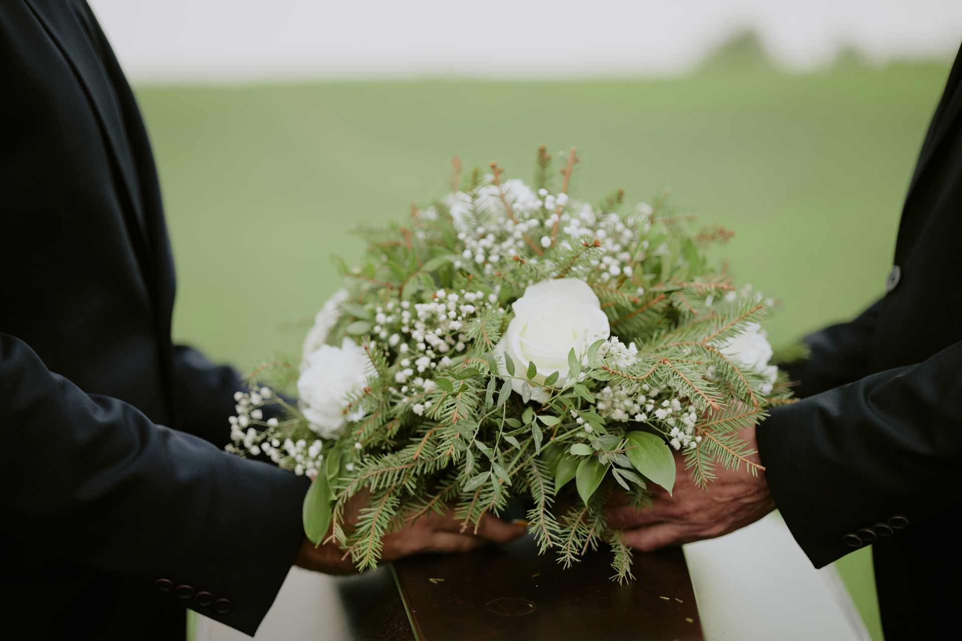 Two people in black coats holding a white floral bouquet outdoors