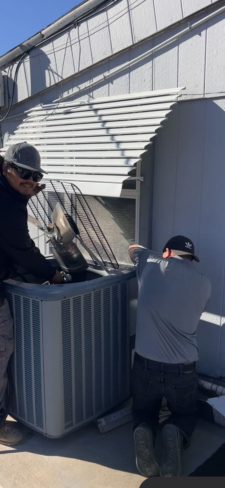 Two Air-Exx technicians servicing a condenser with the grille removed