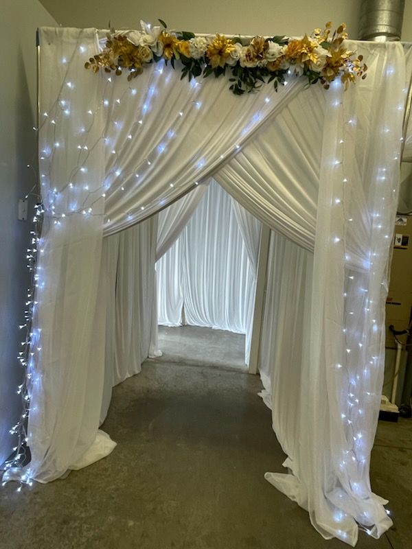 White draped tunnel decorated with fairy lights and flowers.