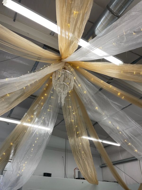 Golden and white fabric drapes from a high ceiling, with a chandelier and fairy lights.
