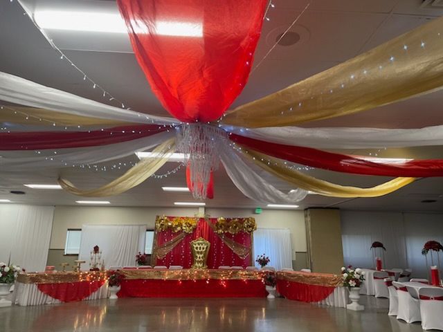 Red and gold draped ceiling decor in a banquet hall, with a decorated stage and tables.