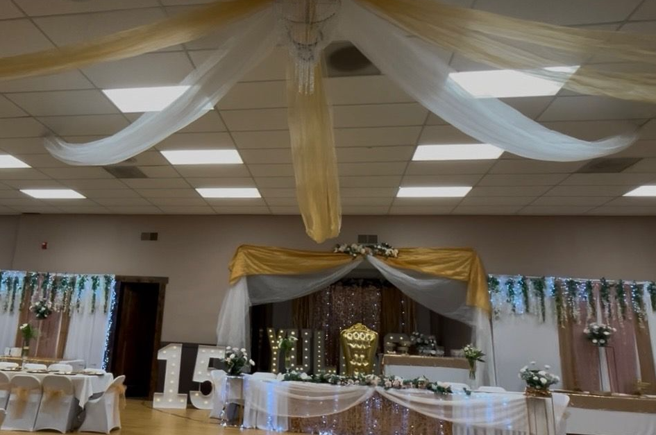 Festive event space with gold and white draping, floral decorations, and a large 