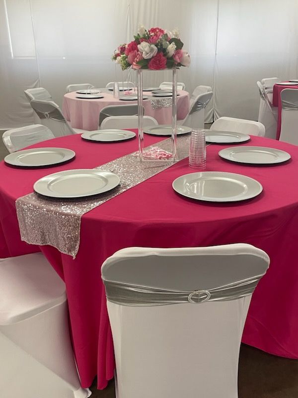 Round table set for event with pink tablecloth, silver plates, floral centerpiece.