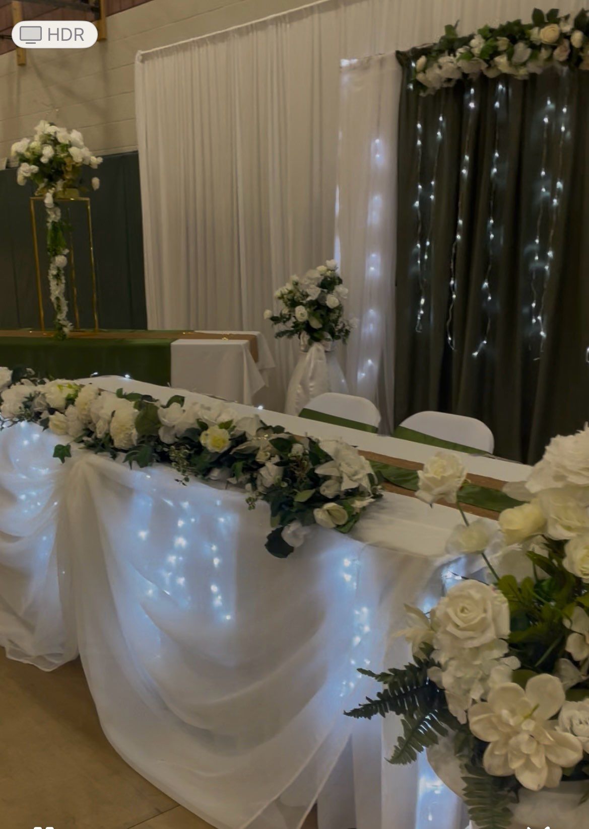 Wedding reception table decorated with white flowers and fairy lights, with olive green accents.