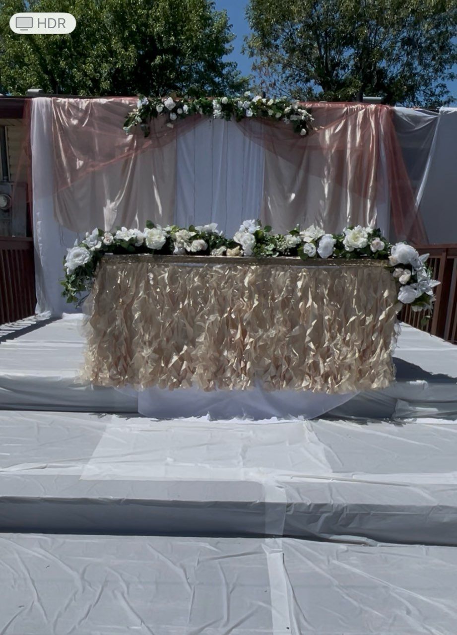 Wedding reception table decorated with white and gold flowers and fabric backdrop.
