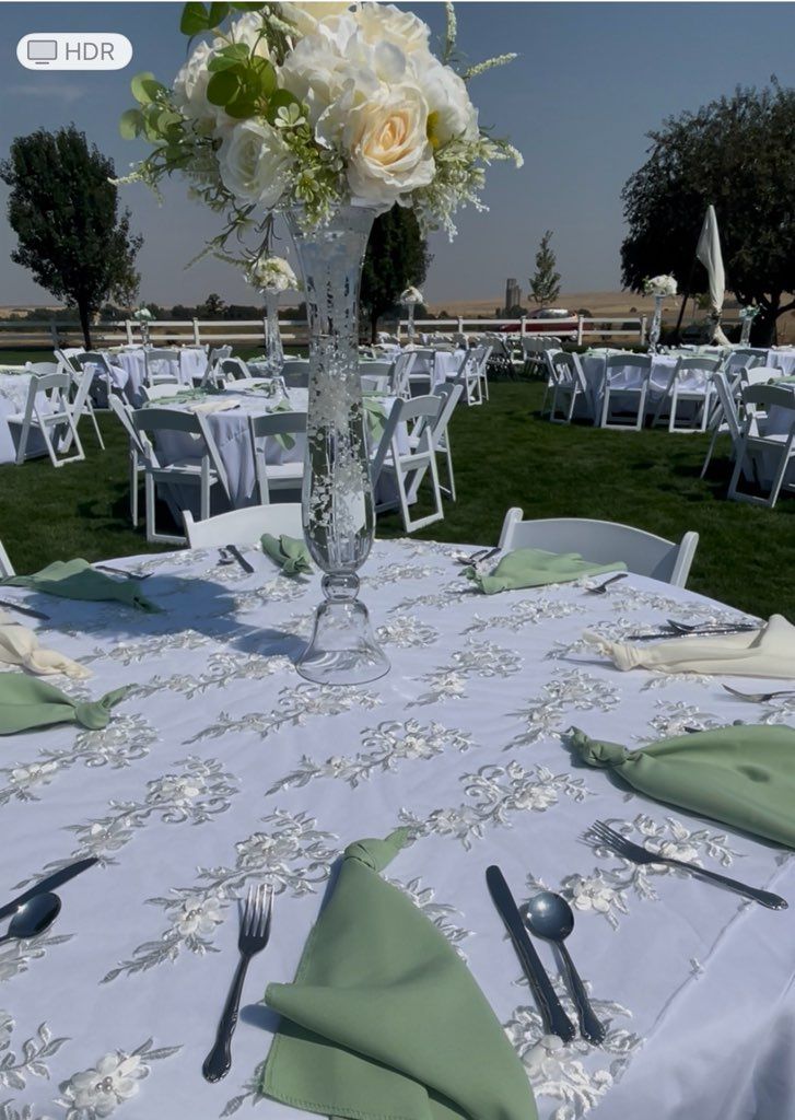 Outdoor reception tables with white linens, floral centerpieces, and green napkins.