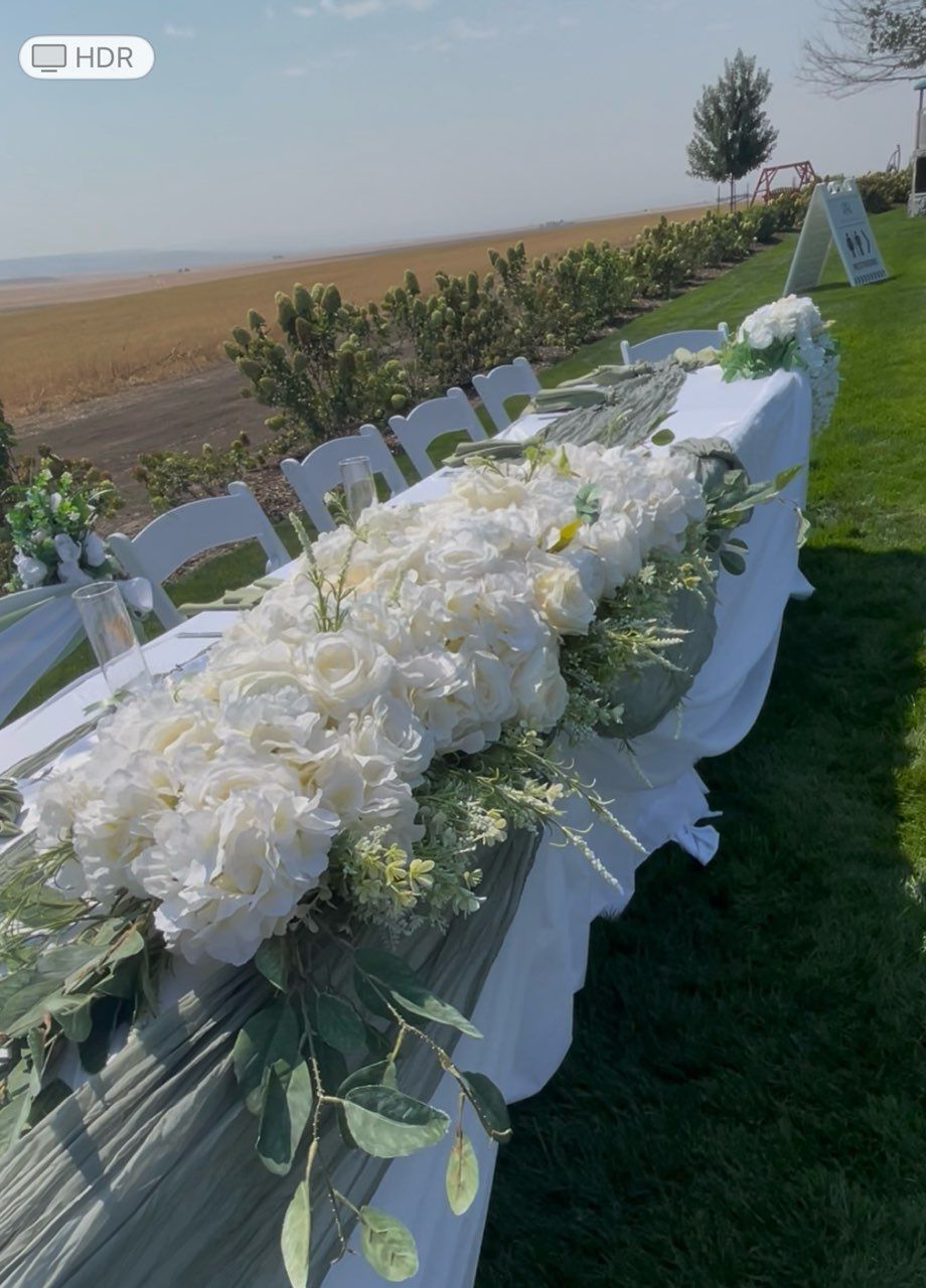 Wedding table decorated with white flowers and greenery overlooking a body of water and field.
