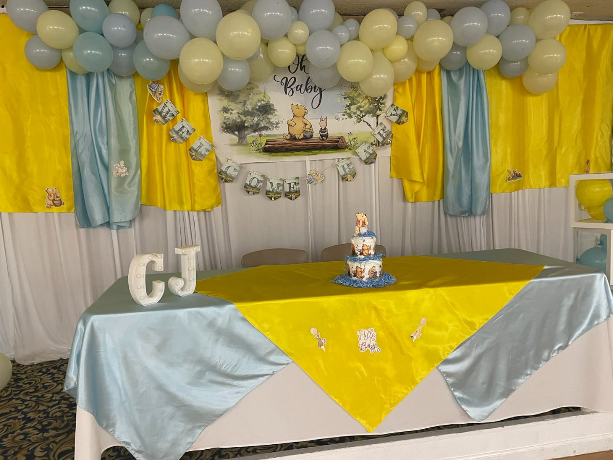 Winnie-the-Pooh themed baby shower. Yellow and blue decor, balloons, cake, and table setting. Banner says 
