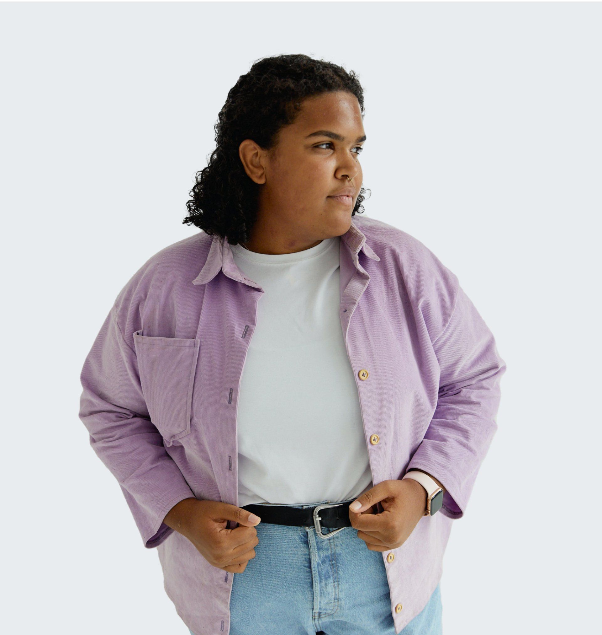 Person in a light purple button-down shirt over a white tee and jeans, looking to the side.