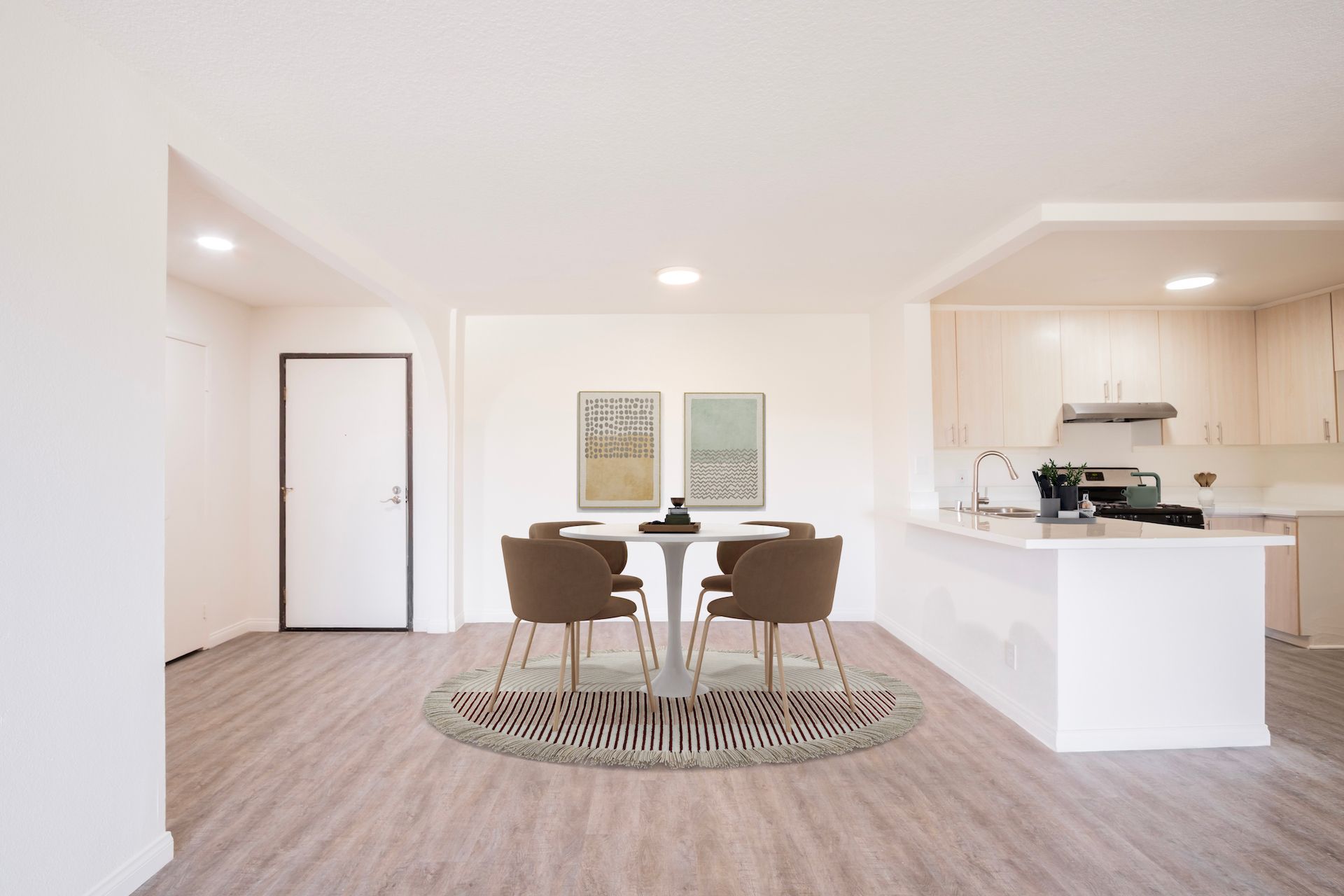 Dining area with table, chairs, and kitchen in light colors. Zebra-print rug on wood floor.