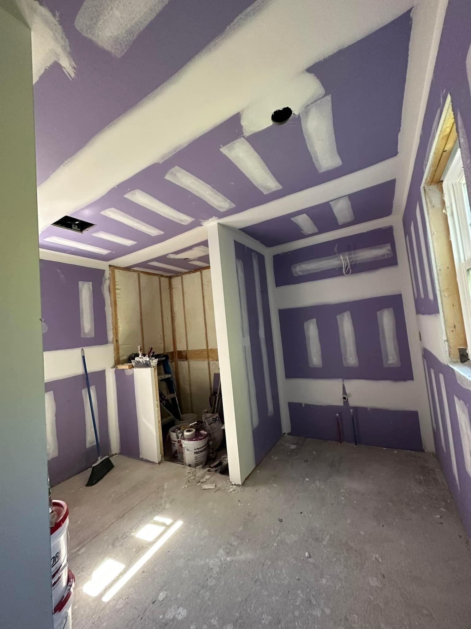A room with purple walls and white trim is being painted.
