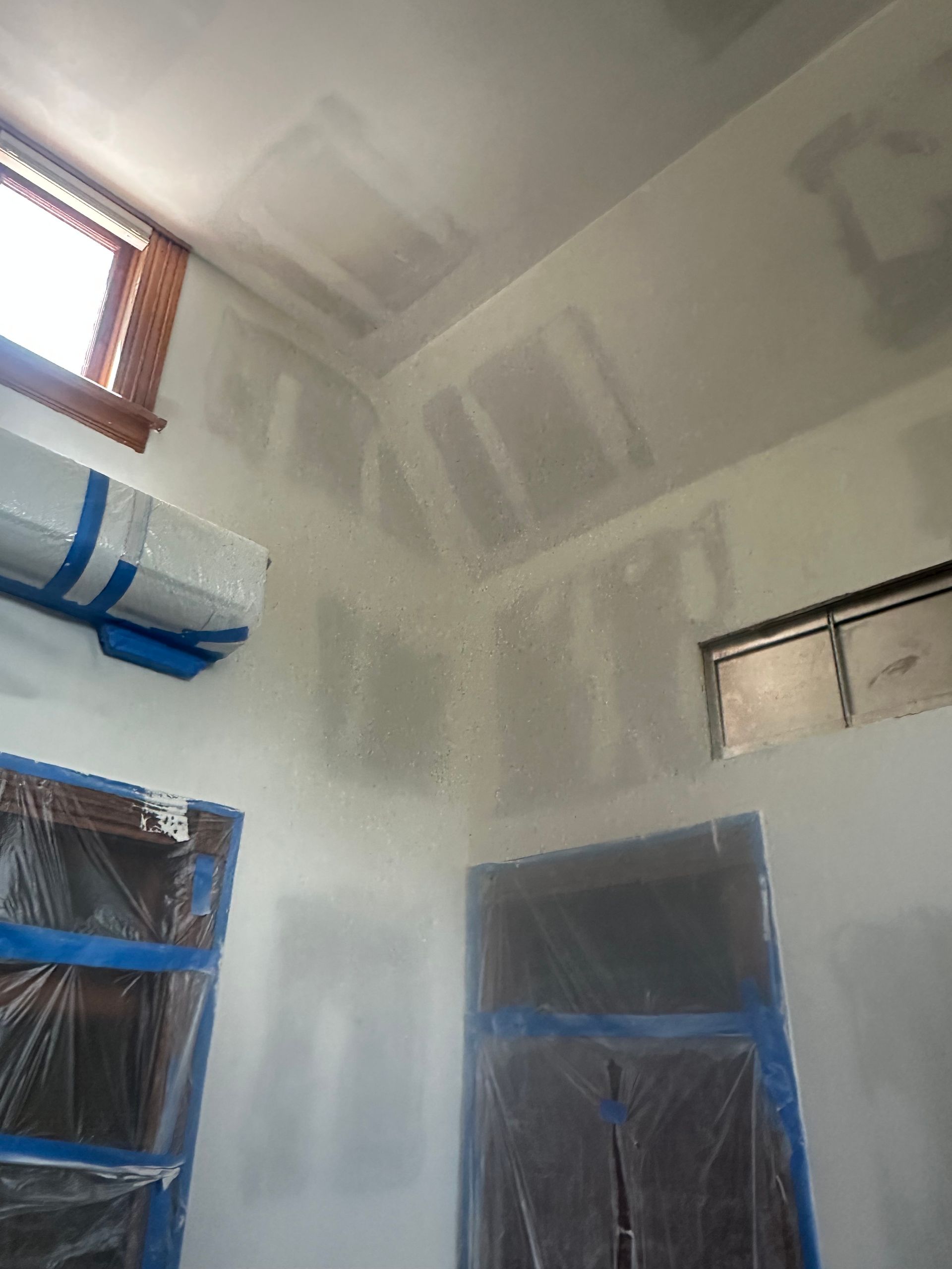 A room with a ceiling that is being painted and a window.