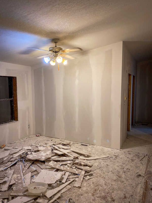A room with a ceiling fan and a lot of pieces of drywall on the floor.