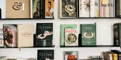 Books displayed on shelves in a cozy café-style shop, with muted green and beige covers.