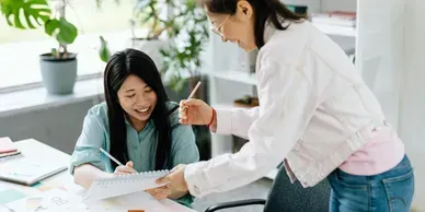 Woman showing paperwork to seated colleague in a bright office