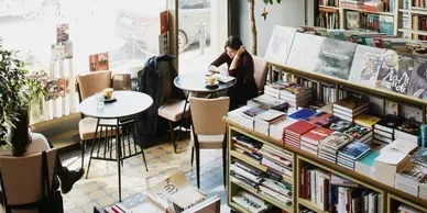 Cozy bookstore cafe with tables, bookshelves, and a person reading by the window.