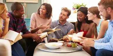 Group of people chatting and sharing food around a table in a bright indoor setting