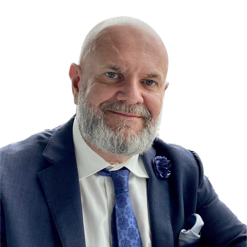 Man in a blue blazer and button-down shirt, looking at the camera against a dark background.