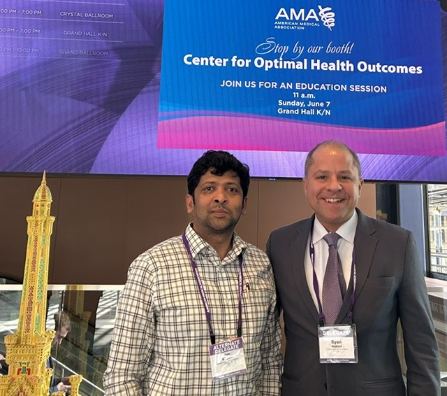 Two men posing at an AMA event in front of a “Center for Optimal Health Outcomes” conference banner
