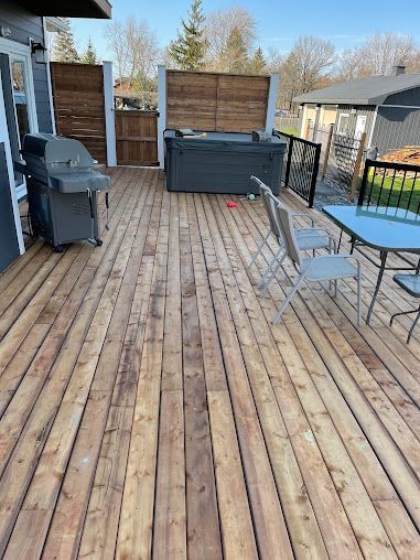 A wooden deck with a hot tub , grill , table and chairs.