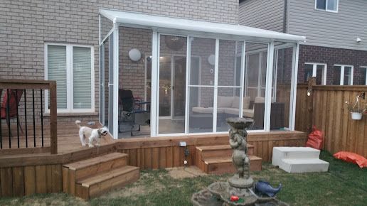 A dog is standing on a deck next to a screened in porch.